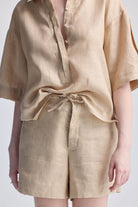 A close-up view of a model wearing reistor Drawstring Shorts in Neutral Beige, showing the adjustable tie waist and natural linen-look texture paired with a matching beige top.