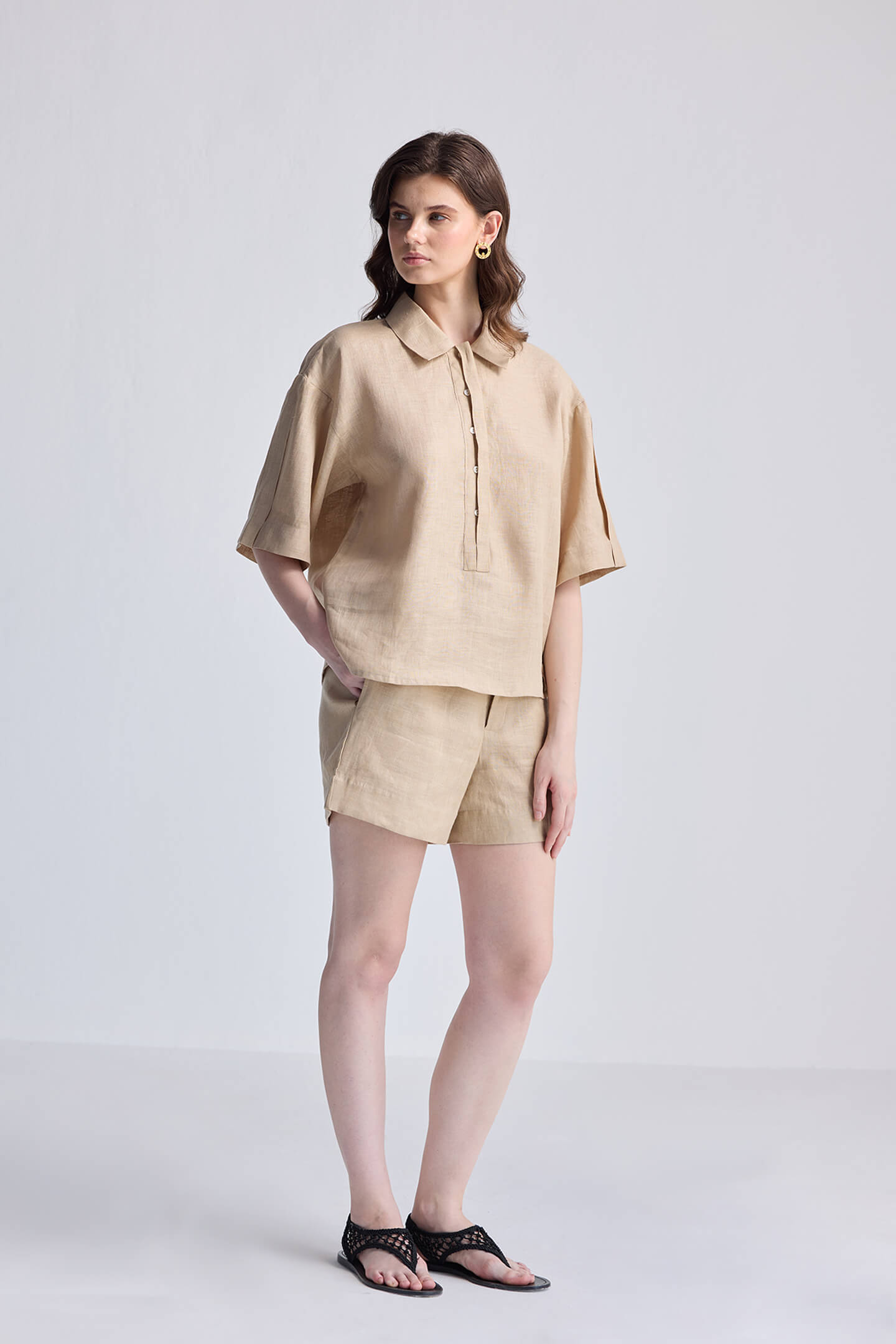 A model showcasing reistor Drawstring Shorts in Neutral Beige paired with a matching short-sleeve linen shirt and black sandals for a sustainable summer look.