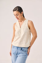 Embroidered Button Front Neck Top in Cream featuring intricate all-over floral embroidery, a sleeveless silhouette, V-neckline with button-front detail, and a relaxed fit, styled with light-wash denim jeans and photographed in a clean studio setting.