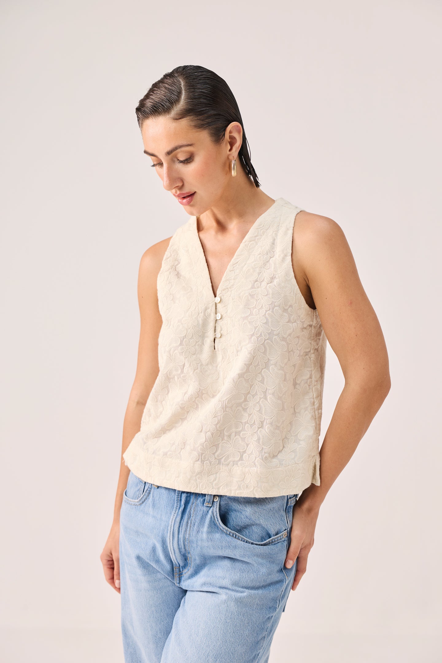 Embroidered Button Front Neck Top in Cream featuring intricate all-over floral embroidery, a sleeveless silhouette, V-neckline with button-front detail, and a relaxed fit, styled with light-wash denim jeans and photographed in a clean studio setting.