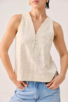Embroidered Button Front Neck Top in Cream featuring intricate tonal floral embroidery, a sleeveless silhouette, and a V-neckline with delicate button-front detailing, shown in a close-up view highlighting the textured fabric and relaxed fit, styled with light-wash denim jeans.