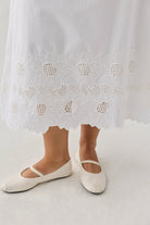 Embroidered Midi Skirt in White featuring a floral eyelet lace hem with scalloped detailing, shown worn with white Mary Jane flats. The skirt falls to mid-calf length and has a light, airy silhouette.