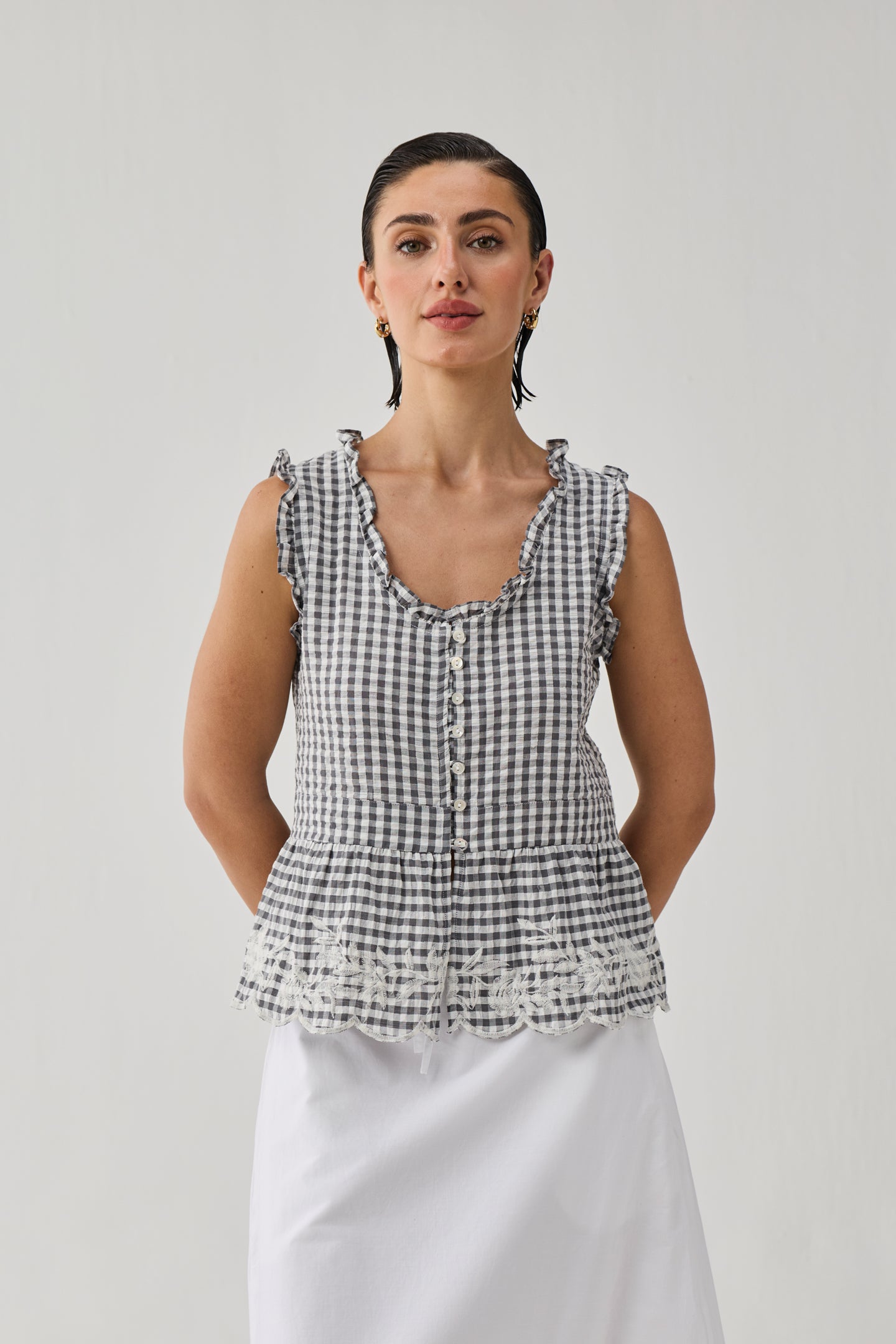 Woman wearing a checkered top and white pants against a plain background