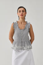 Woman wearing a checkered top and white pants against a plain background