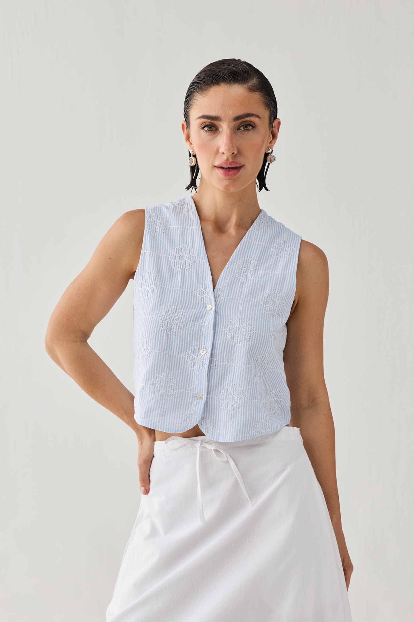 Woman wearing a light blue sleeveless checkered top with a white skirt on a plain background