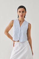 Woman wearing a light blue sleeveless checkered top with a white skirt on a plain background
