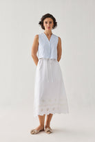 Embroidered Sleeveless Vest Top in Blue Stripe featuring delicate tonal embroidery, a subtle textured stripe pattern, V-neckline, and button-front closure, styled with a white embroidered midi skirt and photographed in a full-length studio portrait.