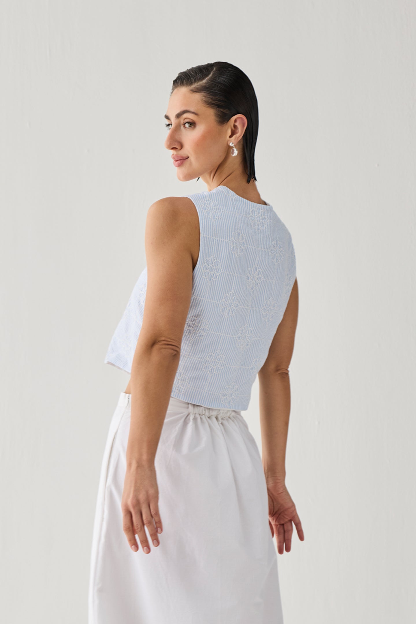 Embroidered Sleeveless Vest Top in Blue Stripe featuring a subtle striped texture, sleeveless cropped silhouette, and round neckline, shown from the back and paired with a white skirt against a clean studio background.
