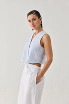 Embroidered Sleeveless Vest Top in Blue Stripe with a textured striped pattern, V-neckline, and cropped sleeveless silhouette, shown from a side angle and paired with a white skirt in a minimalist studio setting.