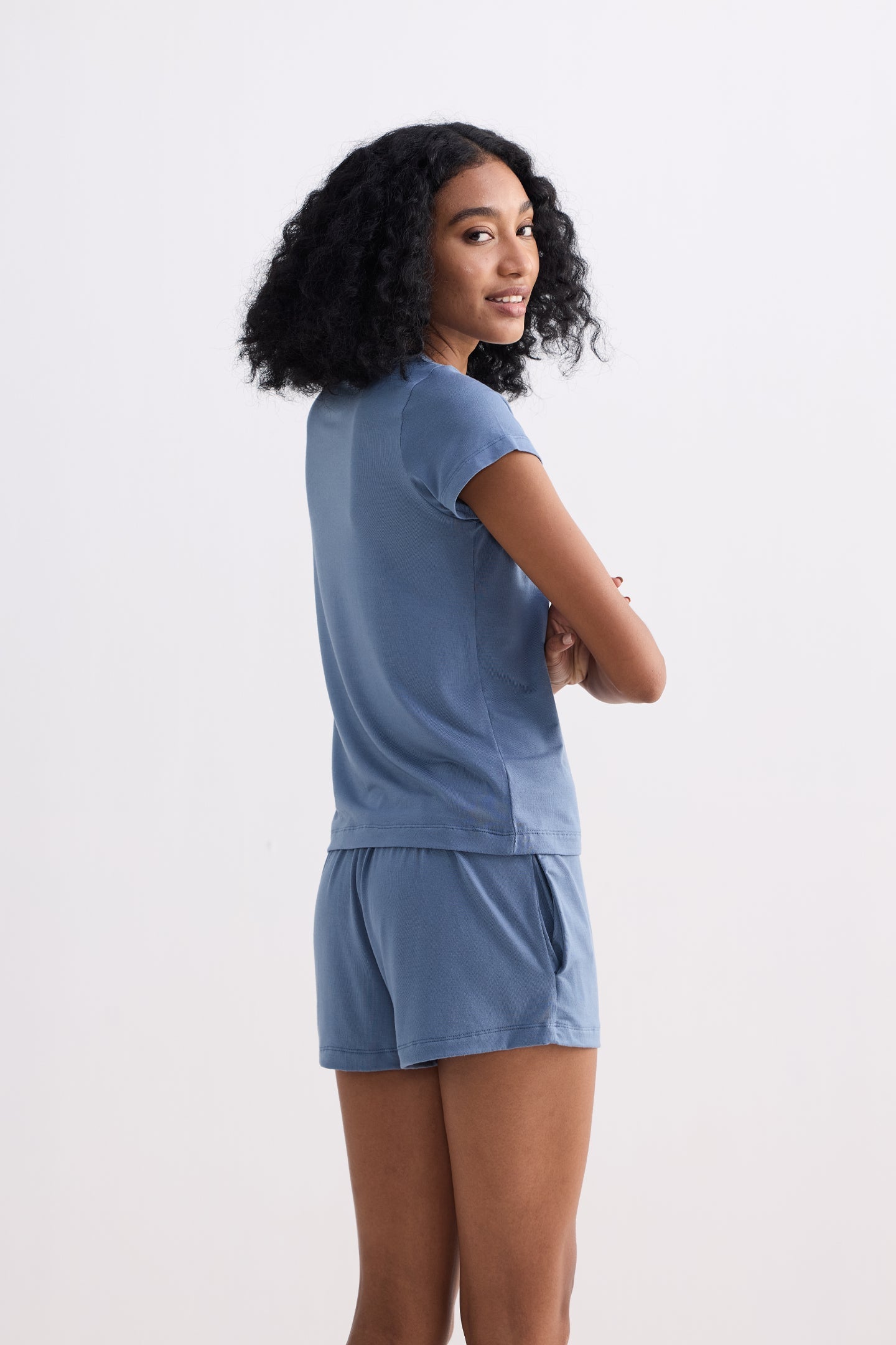 A side-profile studio shot of a model wearing the reistor Essential Short Sleeve Tee Set in Blue, showcasing the lightweight fit of the short-sleeve top and matching comfortable shorts in a soft, sustainable blue fabric.