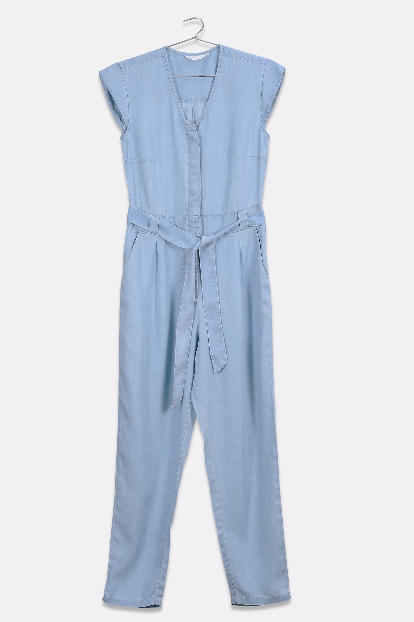 Reistor Evening Chai Jumpsuit in Blue Denim, sleeveless V-neck one-piece with cap sleeves, adjustable tie belt, tapered legs, and sustainable fabric.
