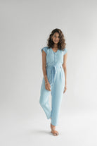 Reistor Evening Chai Jumpsuit in Blue Denim, sleeveless V-neck jumpsuit with cap sleeves, adjustable tie waist, relaxed fit, and sustainable fabric.