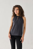 Woman wearing a dark gray sleeveless top with a cutout neckline against a light background