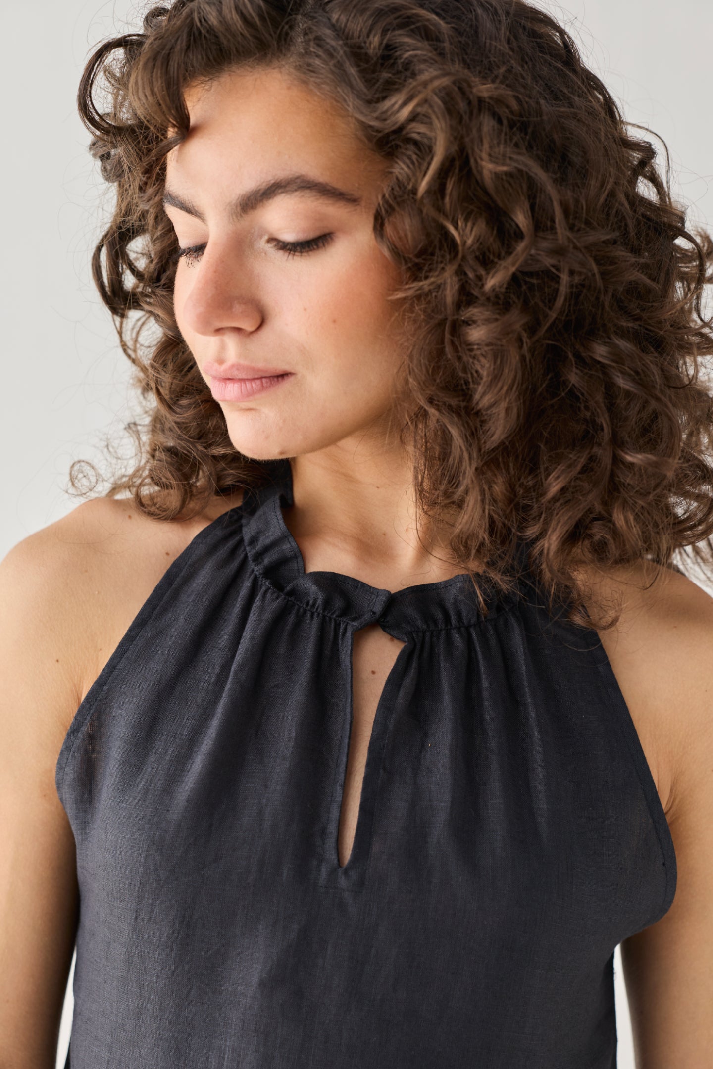 Reistor Halter Neck Top in Black featuring an elegant keyhole opening and softly ruched neckline, captured in a close-up portrait that highlights its refined craftsmanship and timeless appeal.