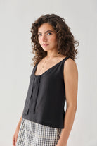 Hemp Front Tie Cami Top in Black featuring a relaxed silhouette, V-neckline with front tie detail, and sleeveless design. The model is shown from the front wearing the lightweight, breathable hemp top with a check-pattern skirt.