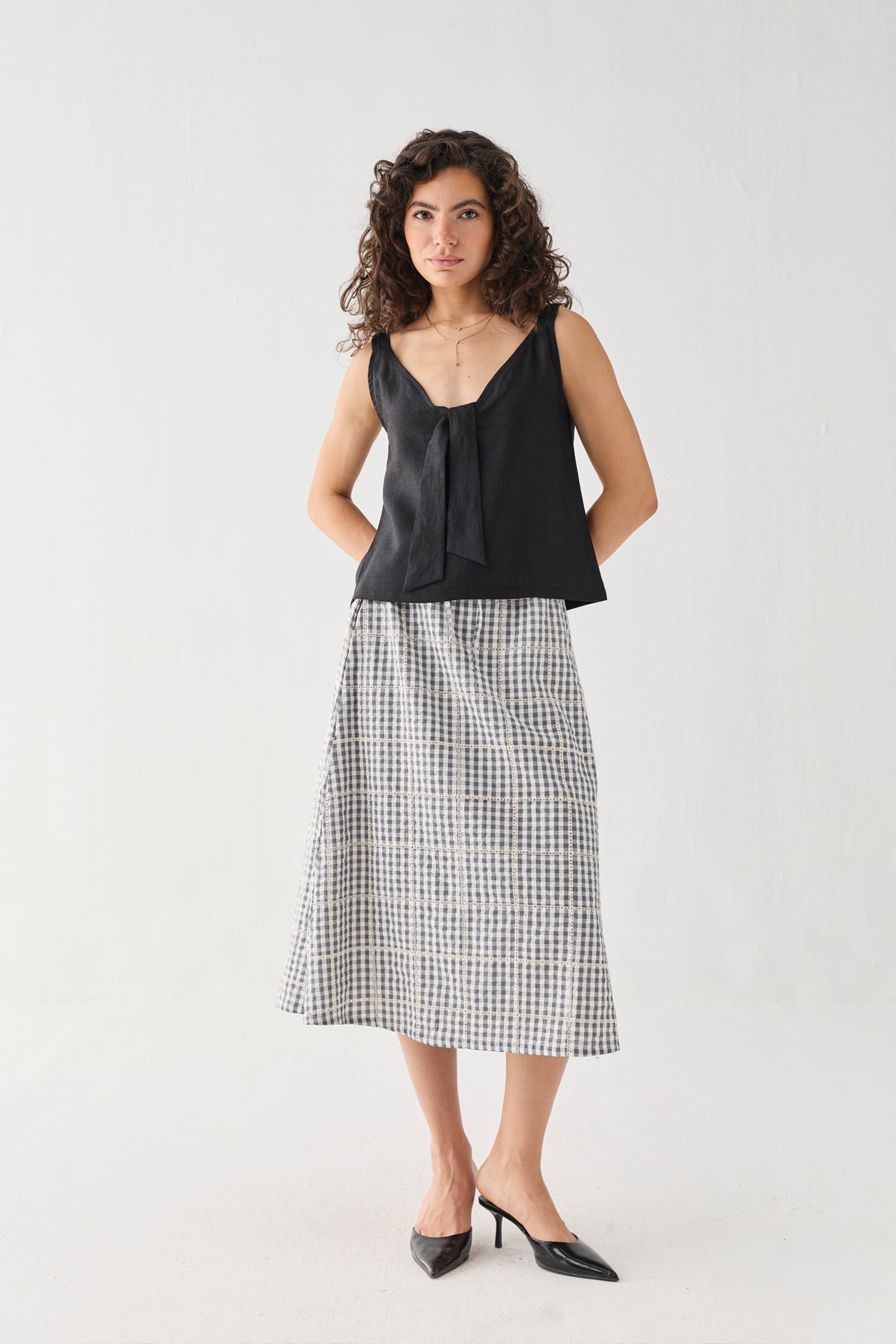 Full-length view of the Hemp Front Tie Cami Top in Black, featuring a relaxed fit, sleeveless design, and statement front tie detail. Crafted from breathable hemp fabric, the top is styled with a check-pattern midi skirt for an effortless, everyday look.
