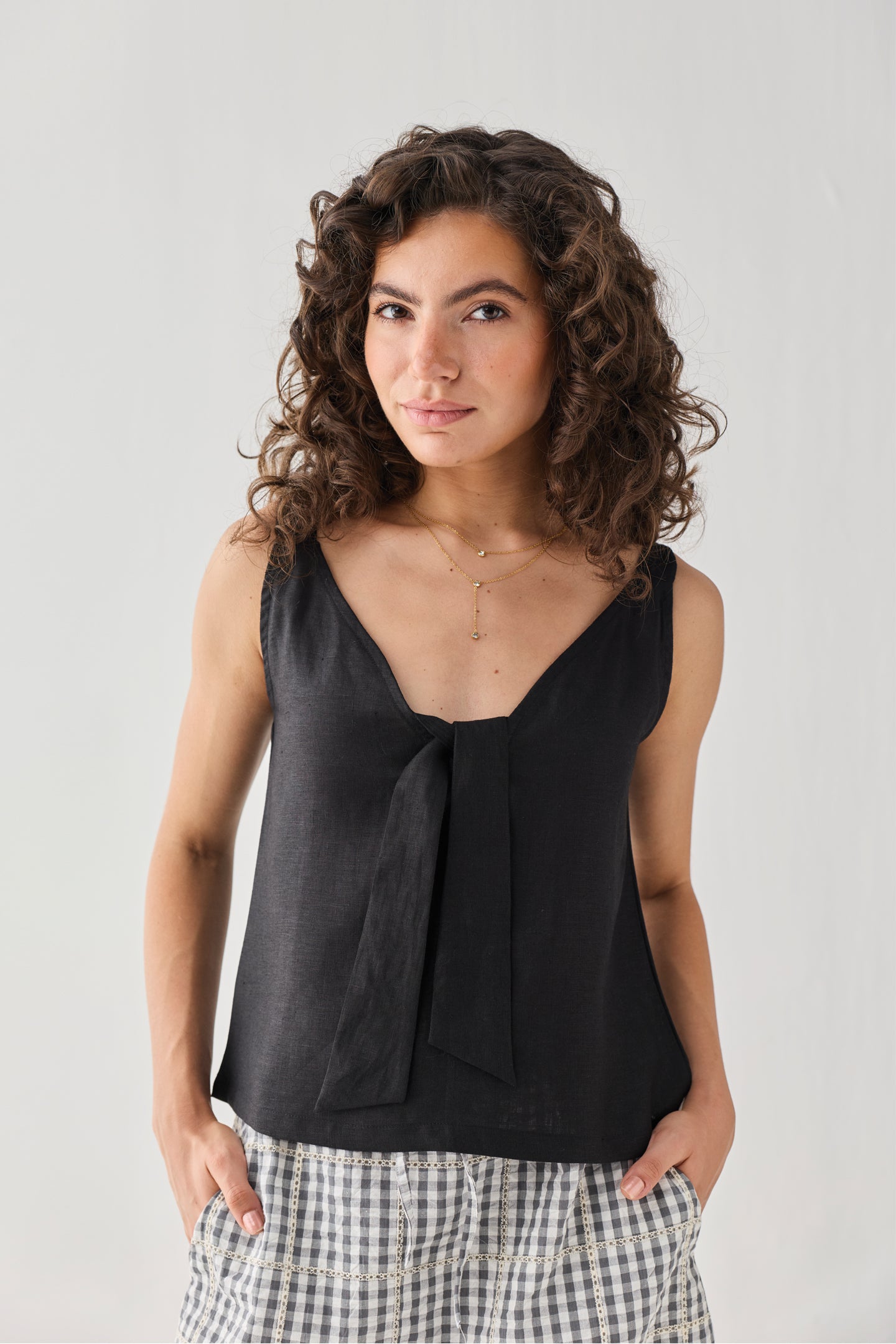 Woman wearing a black sleeveless top with a knot detail against a plain background