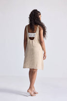 Model wearing the reistor Hemp Short Dress with Back Embroidered Lace Detail, featuring a natural beige hemp fabric, sleeveless silhouette, open back design, and delicate embroidered lace, styled with minimal heels.