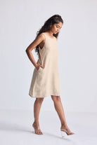 Model wearing the reistor Hemp Short Dress with Back Embroidered Lace Detail in natural beige hemp fabric, sleeveless A-line silhouette with side pockets, styled for a minimal sustainable fashion look.