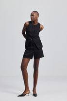 A full-body studio shot of a model wearing the reistor Hemp Vest Jacket Set in Black, featuring a tailored button-up sleeveless vest and matching high-waisted shorts, styled with black pointed-toe kitten heel mules.