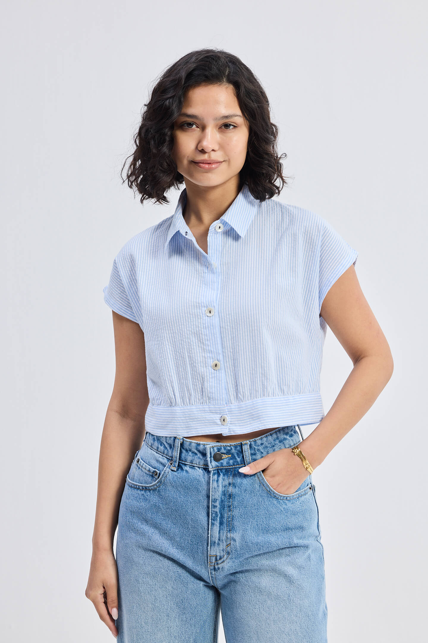A woman wearing an oversized crop shirt with classic stripes, in a light solid color, paired with blue jeans.