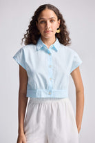 A woman modeling an oversized crop shirt in summer blue with a cinched waist, made from organic cotton.