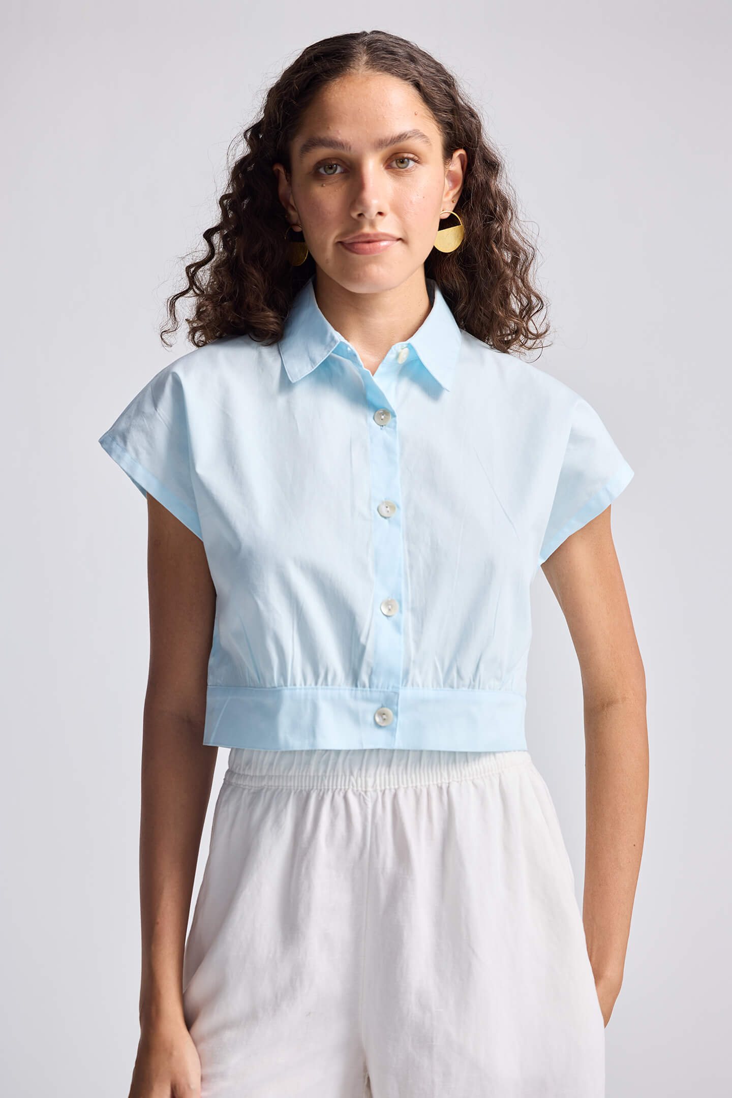 A woman modeling an oversized crop shirt in summer blue with a cinched waist, made from organic cotton.