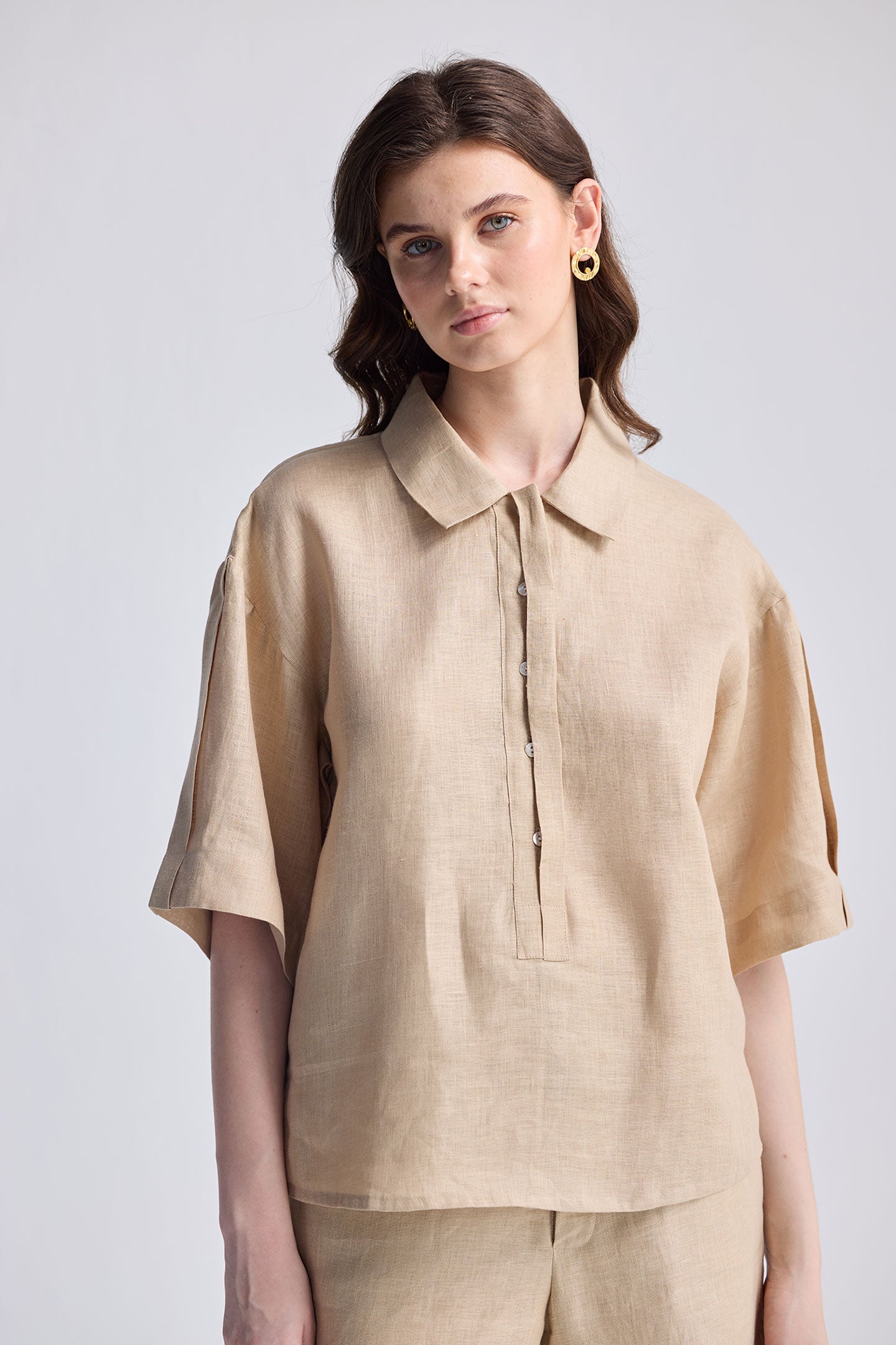 Woman wearing the Oversized Flowy Shirt in Neutral Beige, a lightweight linen-texture button-up with short sleeves and a relaxed fit, styled with matching trousers.