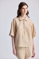 Woman wearing the Reistor Oversized Flowy Shirt in Neutral Beige, a lightweight linen-texture button-up with short sleeves and a relaxed fit, styled with matching pants.