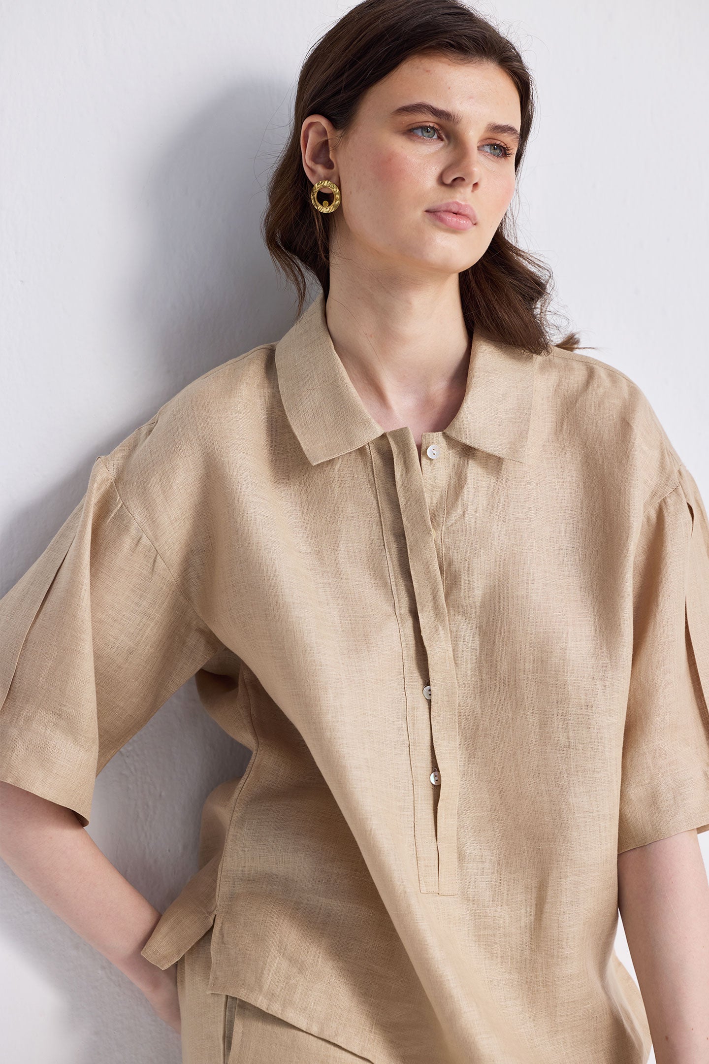 Woman modeling the Reistor Oversized Flowy Shirt in Neutral Beige, a relaxed-fit linen button-up with short sleeves and a classic collar, paired with matching pants on a white background.