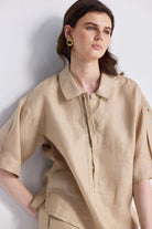 Woman modeling the Reistor Oversized Flowy Shirt in Neutral Beige, a relaxed-fit linen button-up with short sleeves and a classic collar, paired with matching pants on a white background.