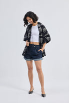 Woman wearing Oversized Shirt with Front-ties in Animal Print by reistor, styled over a white top with denim shorts on a clean white background.