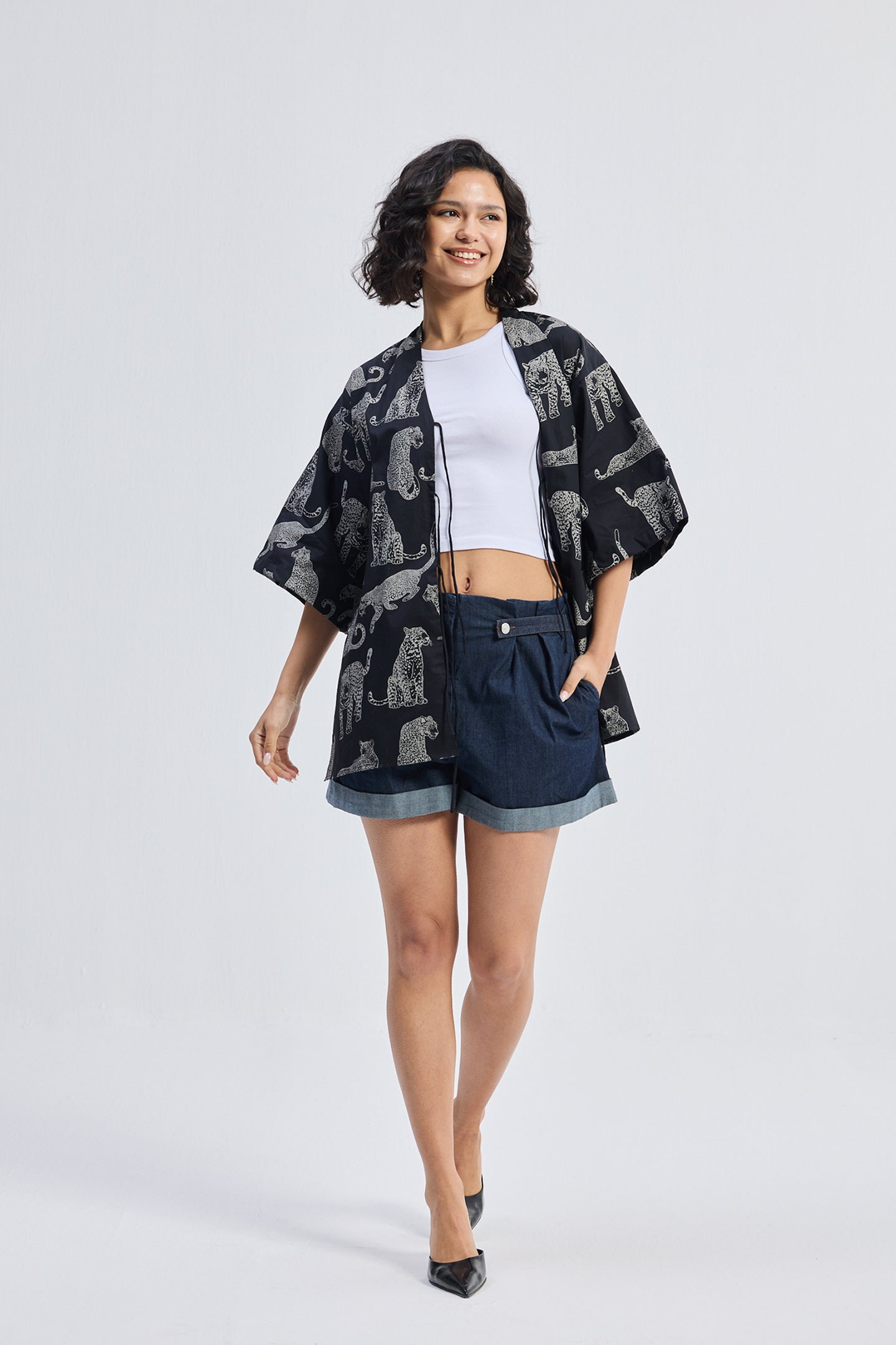 Woman walking in Oversized Shirt with Front-ties in Animal Print by reistor, styled with a white top and denim shorts on a white background.