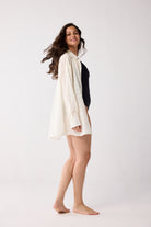 Woman wearing a white cover-up over a black swimsuit on a white background