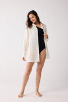 Woman wearing a white shirt over a black swimsuit on a white background