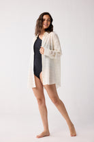 Woman wearing a white cover-up over a black swimsuit on a white background