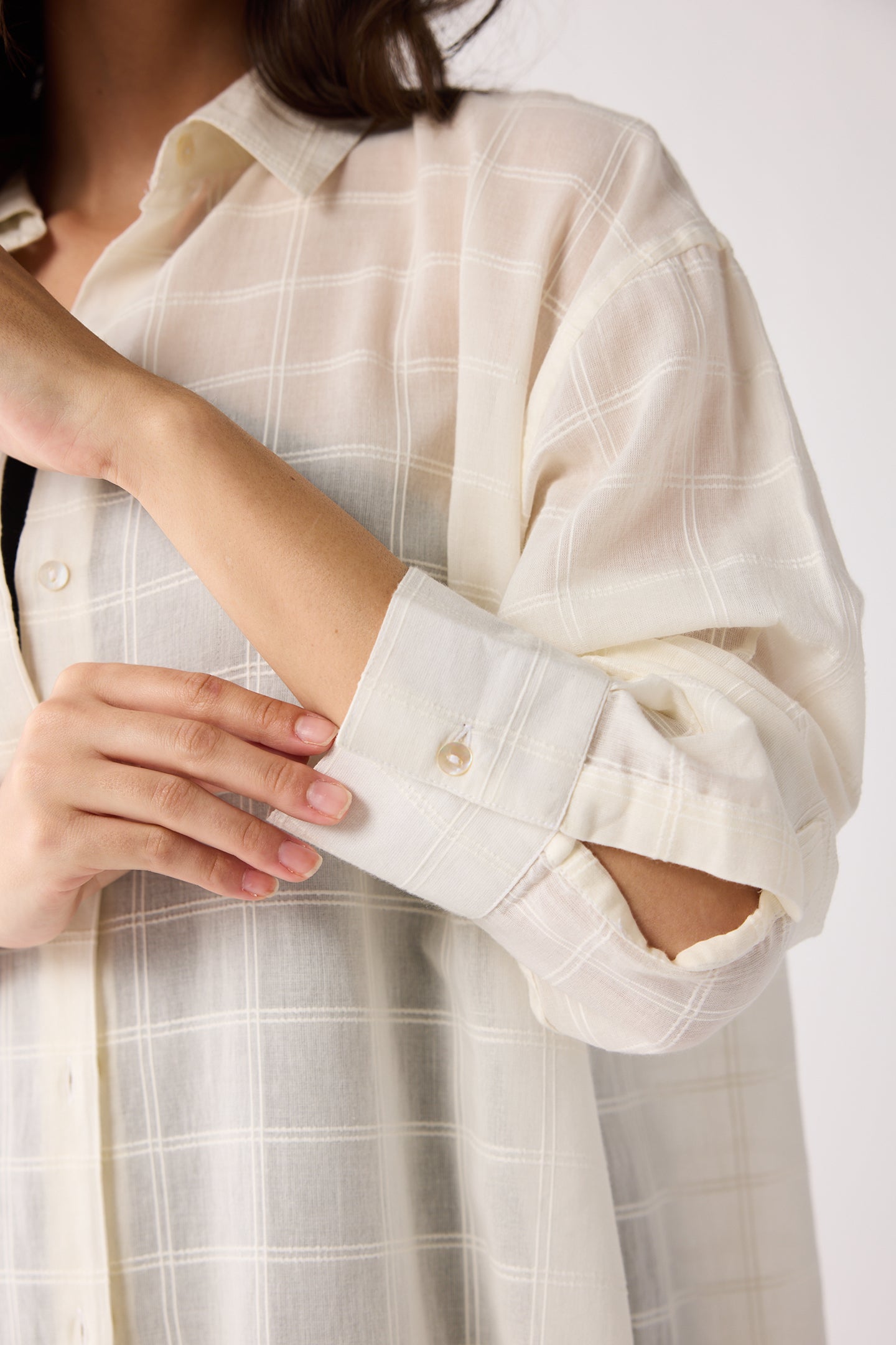 Person wearing a light-colored checkered shirt with rolled-up sleeves on a white background