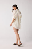 A woman wearing a white shirt and black sandals on a plain background