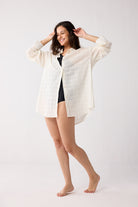 Woman wearing a white sheer jacket over a black top on a white background