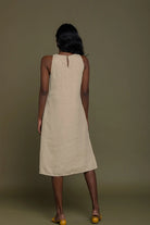 Woman wearing a beige sleeveless dress against a brown background