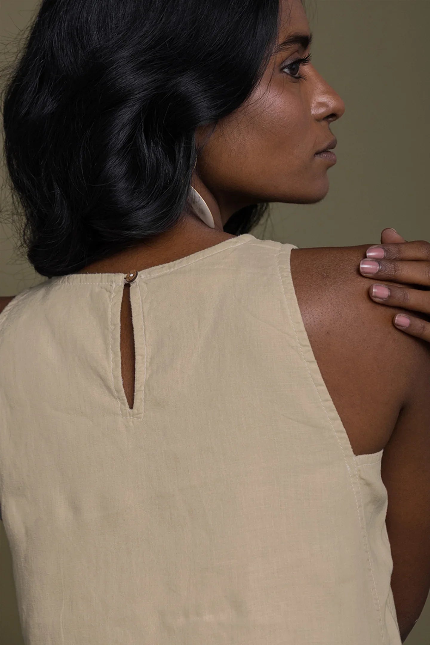 Woman wearing a Reistor beige sleeveless top with a cutout detail on a plain background.