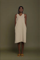 Woman wearing Reistor Reading Tea Leaves Dress in Neutral Beige, a sleeveless V-neck midi dress with side pockets.