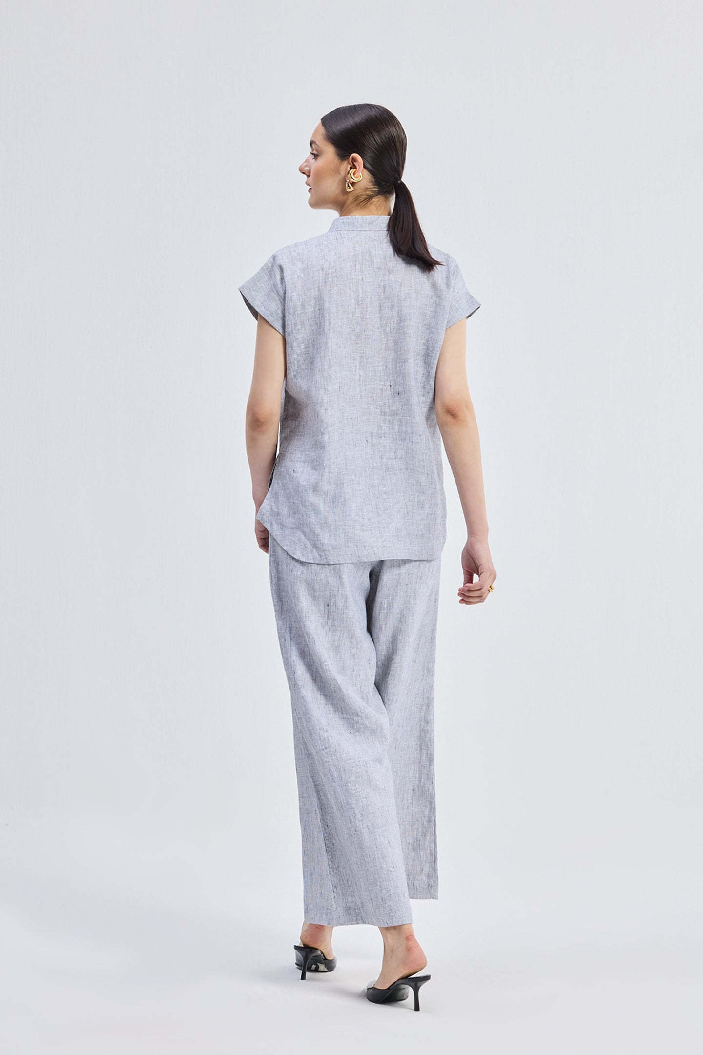Back view of the Relaxed-fit Shirt Set in Linen Stripes by reistor, showing the seamless pinstripe pattern and relaxed fit of the sustainable linen shirt and trousers.