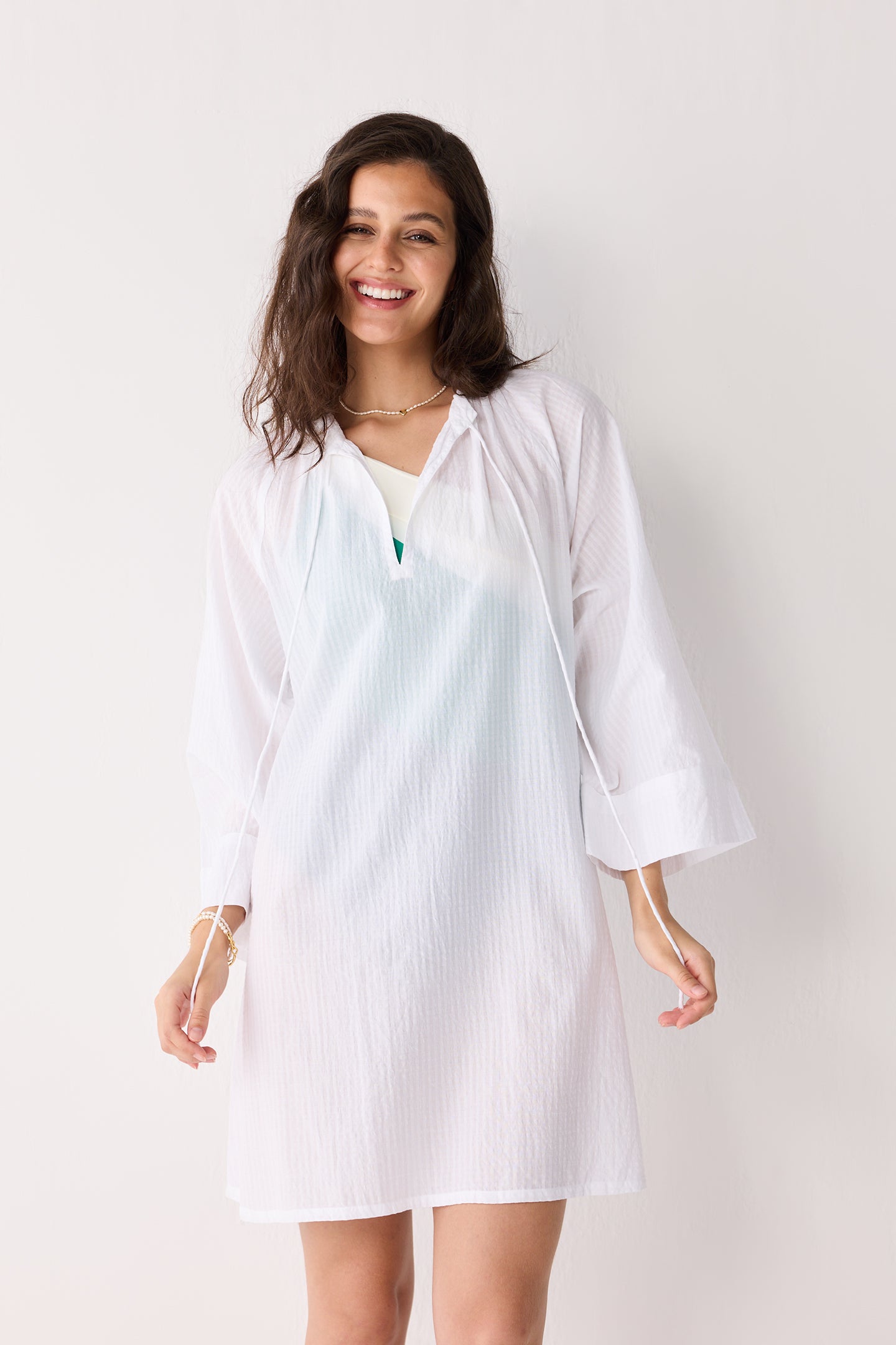 A woman wearing a white beach cover-up with a plain background