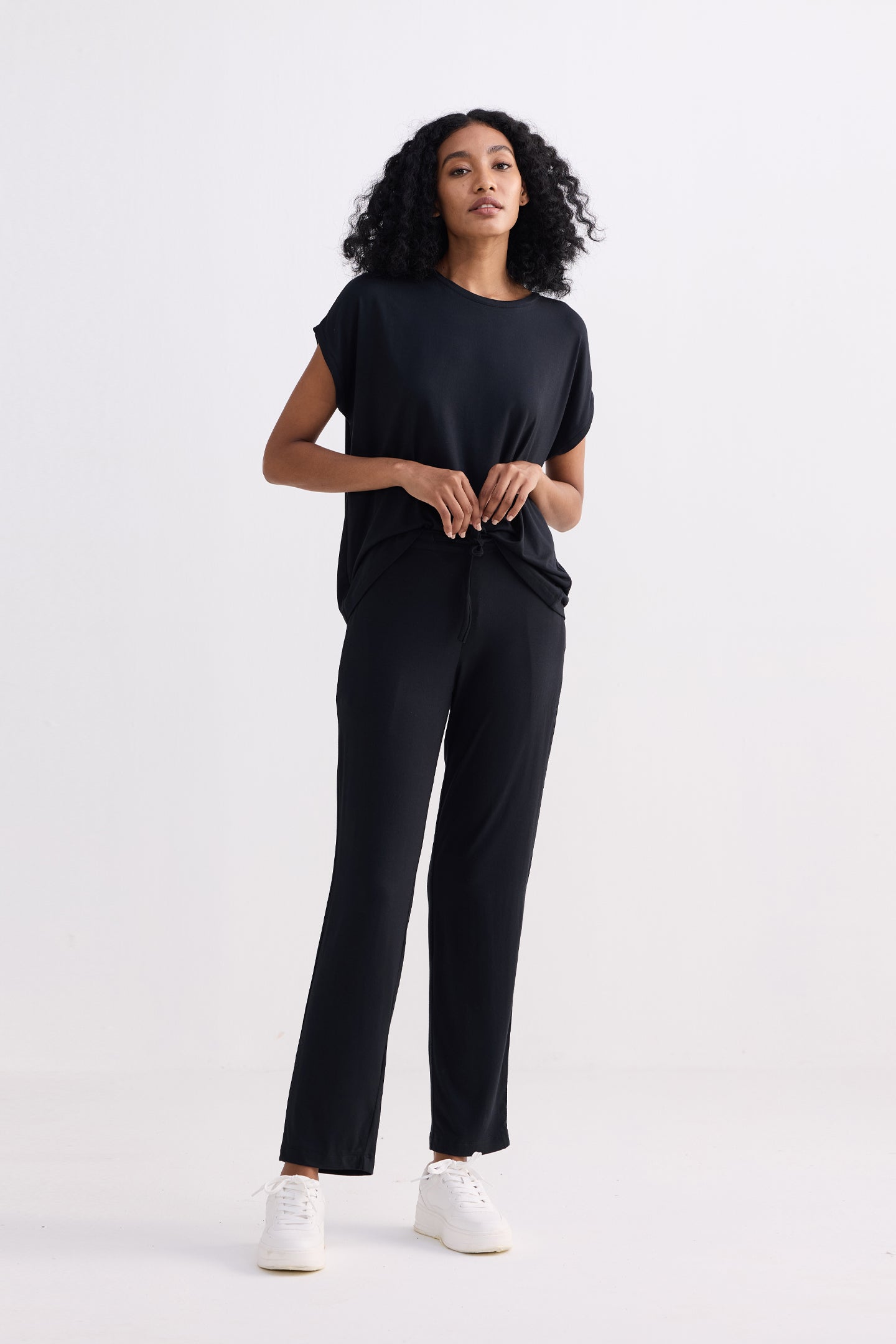 A minimalist studio portrait of a model wearing the reistor Relaxed Tee Set in Black, featuring an oversized sustainable t-shirt tucked into matching fluid-fit trousers for a modern loungewear look.