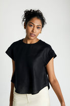 Woman wearing the Reistor Sandcastle Saturdays Top in Black, featuring cap sleeves, a shirttail hem, and a relaxed fit for effortless sustainable everyday style.