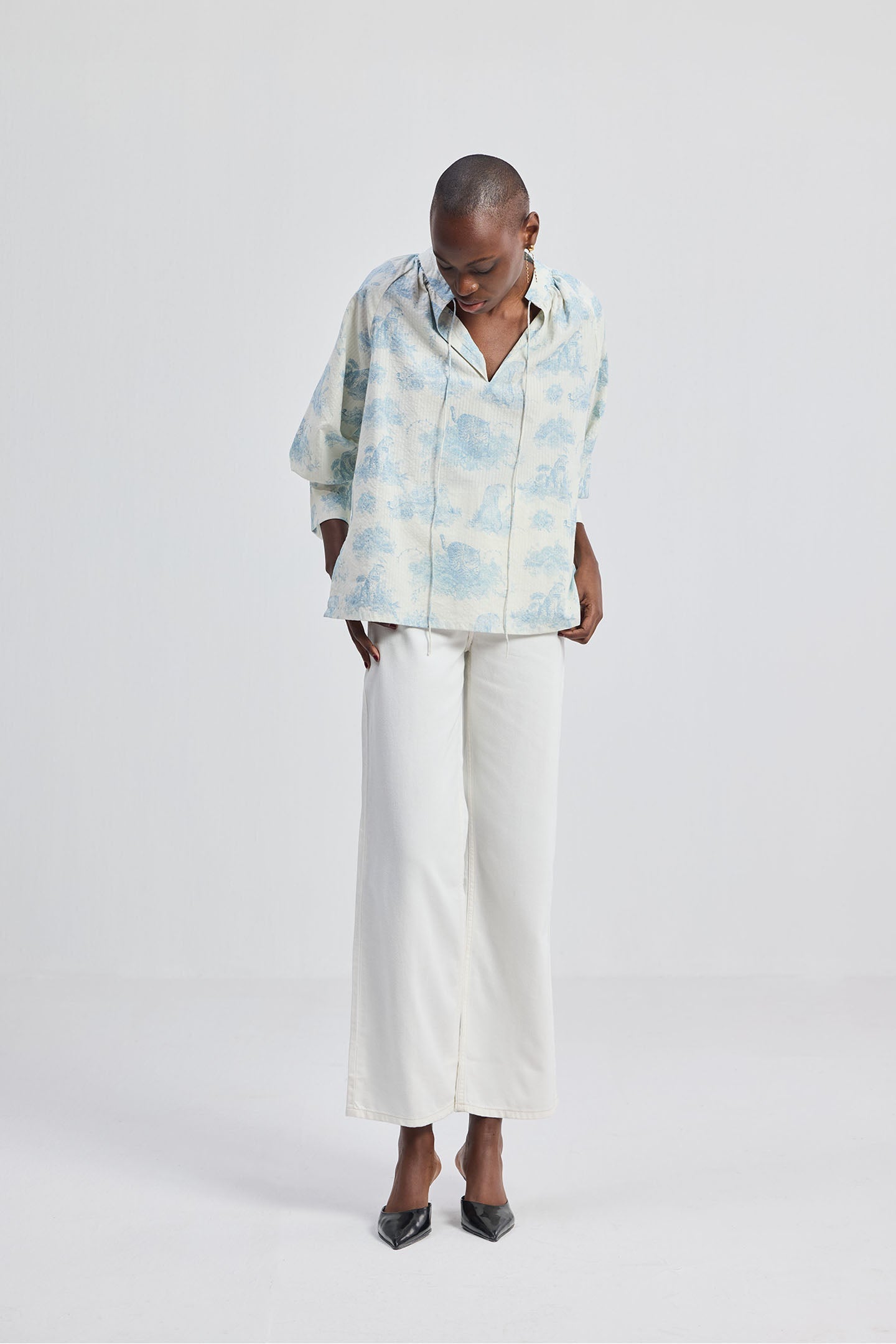 Front view of a model wearing the reistor Relaxed-fit Shirt with Drawstring in Animal Print, styled with white wide-leg pants and heels on a clean studio background.