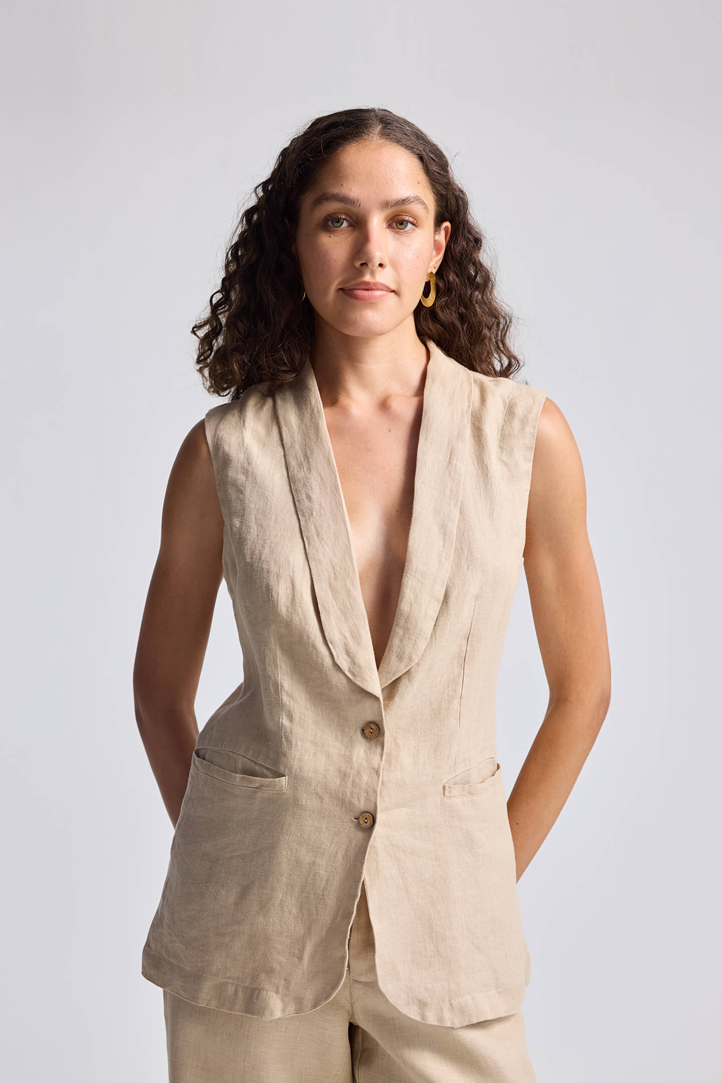 Front view of model wearing Reistor Sleeveless Hemp Jacket in beige, featuring a deep V-neckline, button-front closure, and tailored fit.