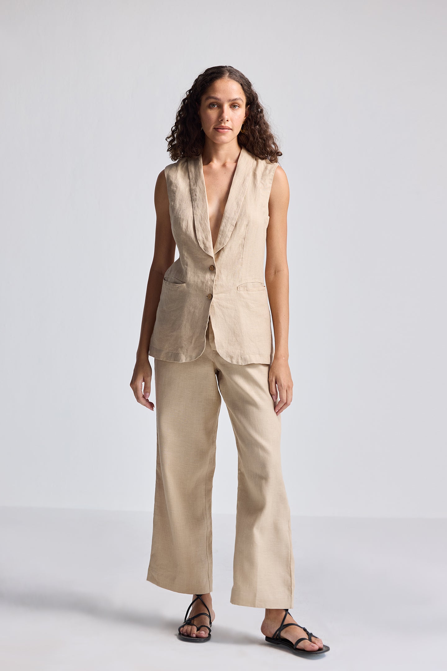 Full-length studio shot of model wearing Reistor Sleeveless Hemp Jacket Set in natural beige, featuring a sleeveless tailored hemp jacket with button detailing paired with wide-leg hemp trousers for sustainable women’s fashion.