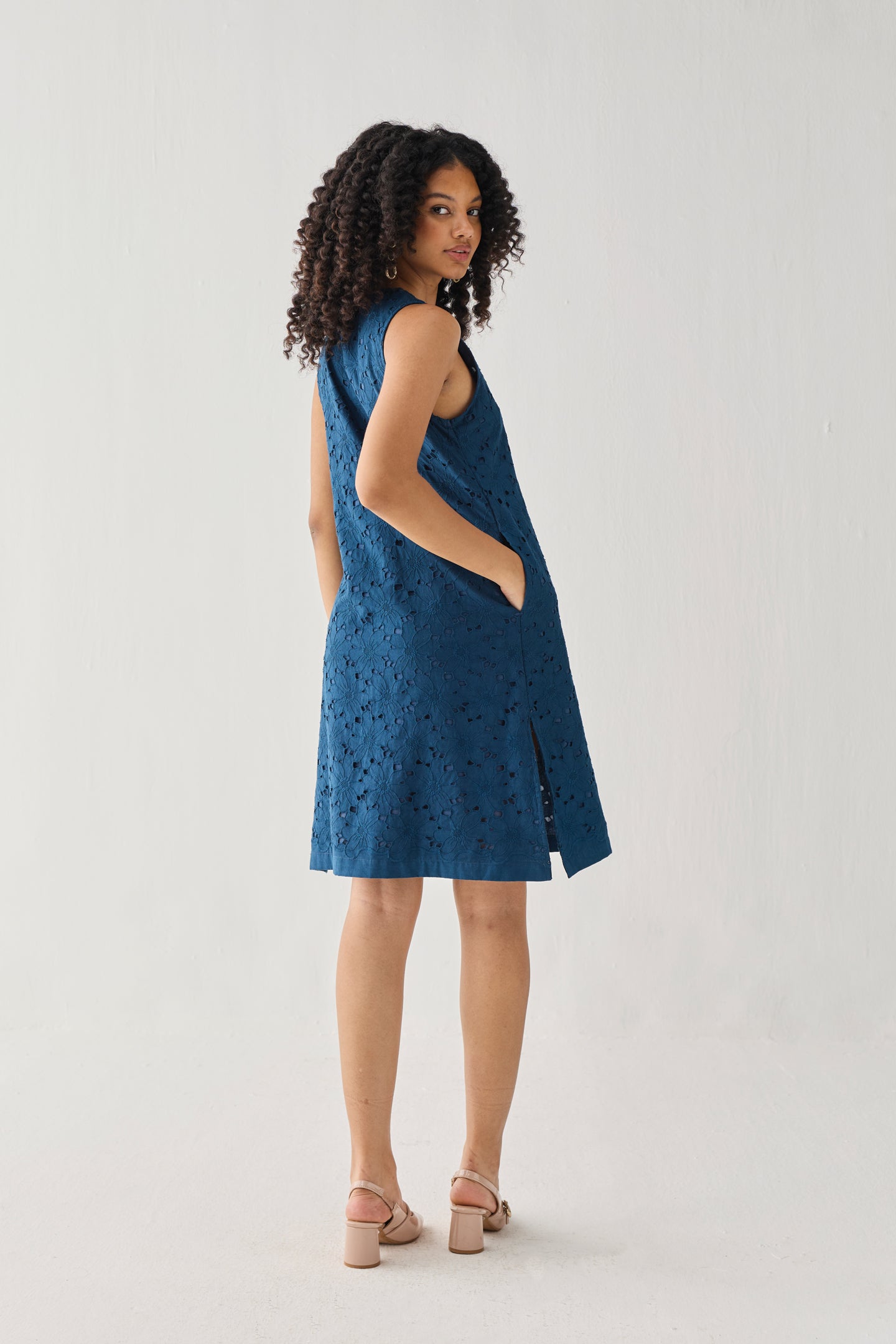 Sleeveless Knee-Length Dress in Blue featuring an all-over embroidered eyelet pattern, relaxed A-line silhouette, and practical side pockets, shown from the back in a full-length studio portrait.